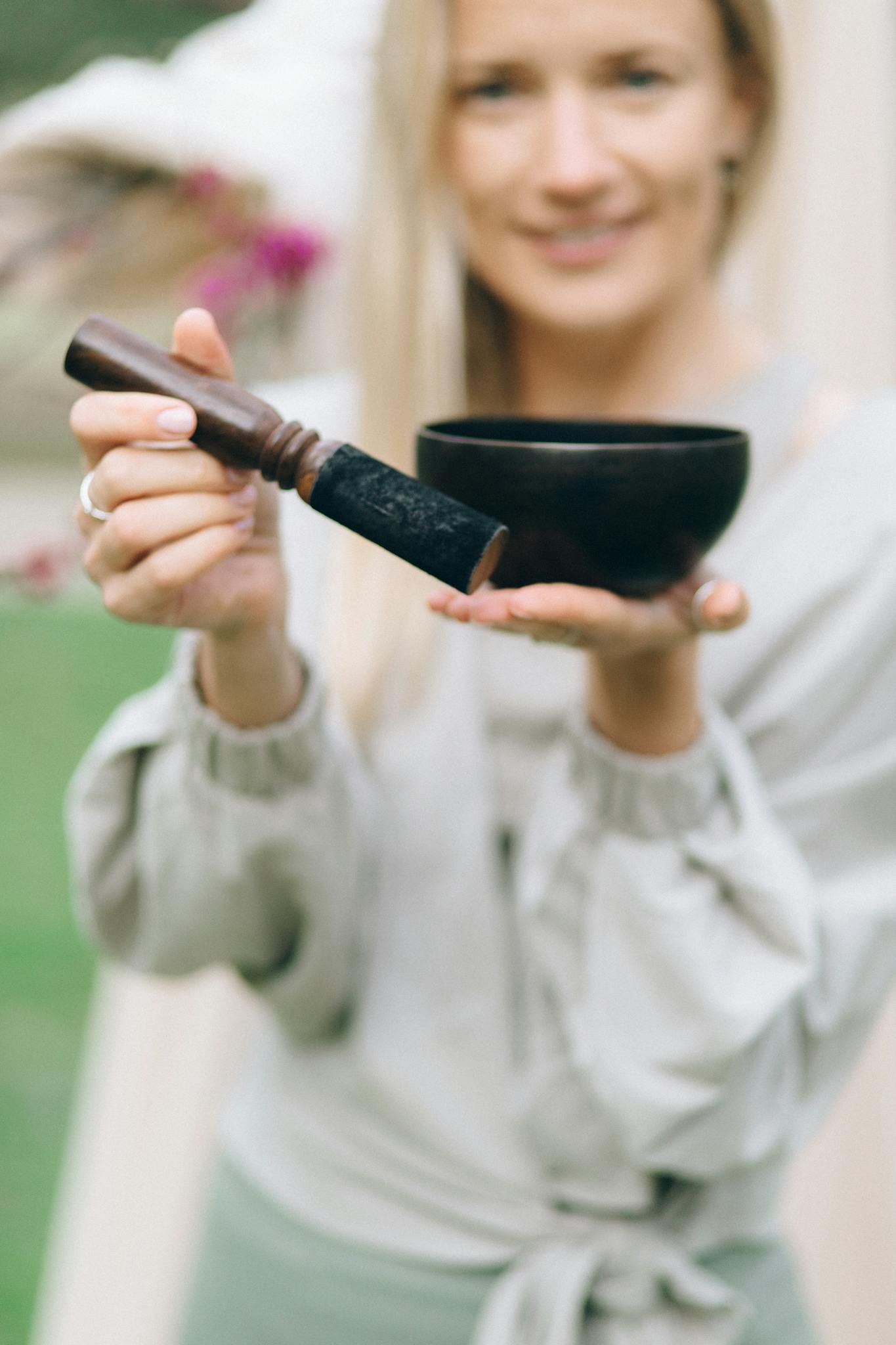 Close-up of a woman holding a singing bowl, symbolizing peace and relaxation outdoors.