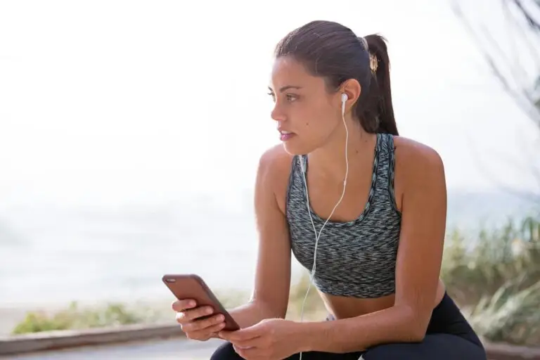 Fit woman with earphones and smartphone taking a break during an outdoor workout.