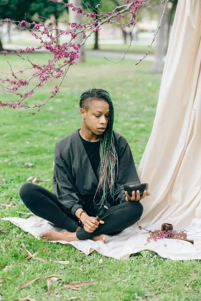 Young woman meditating in a park, holding a tablet. Serene nature setting.