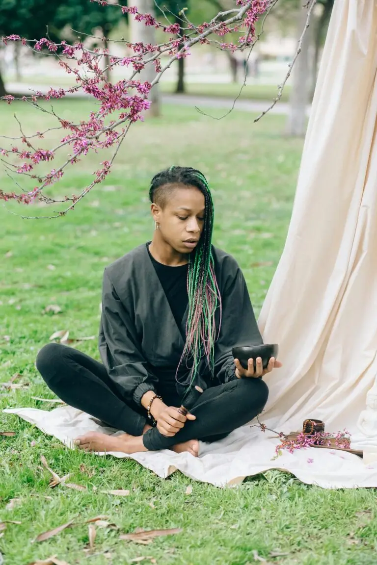 Young woman meditating in a park, holding a tablet. Serene nature setting.